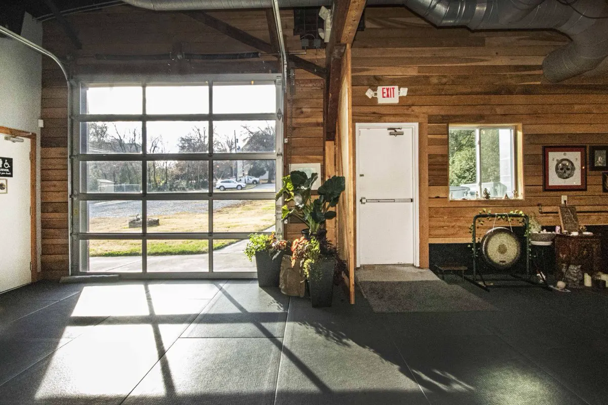 A studio corner with a glass garage door, plants and a gong on a stand